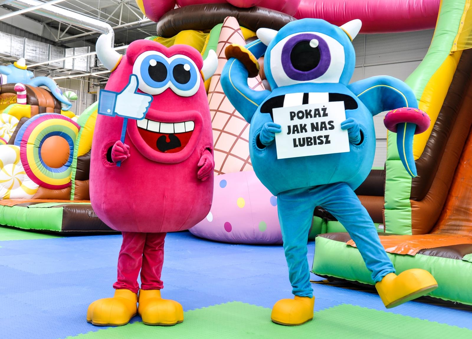 Fotografia przedstawia maskotki monster Andy i Candy stojące z planszami zawierającymi komunikaty dla fanów Candy Parku